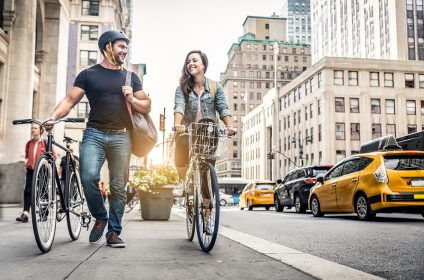 A man and a woman with bicycles on a city street, surrounded by taxis and tall buildings