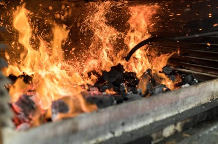 Roaring fire on a barbecue grill with charred coals and sparks in a high heat cooking setup