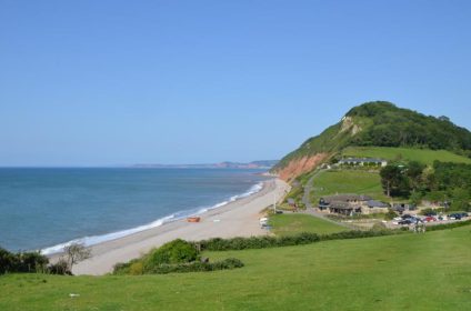 Scenic view of a tranquil beach with lush green hills and clear blue sky in the UK coastline landscape