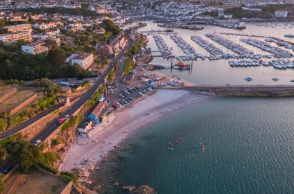 Aerial view of a coastal town with marina, beach, and kayakers in the water at sunset in the UK