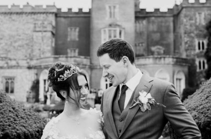 Bride and groom smiling in front of a historic castle, celebrating their wedding day in elegant attire