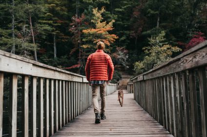 Man in red jacket walking dog on forest bridge during autumn
