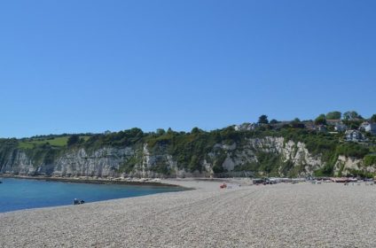 Pebble beach with lush cliffs and houses in Beer, Devon, under a clear blue sky in the background