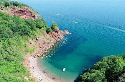 Aerial view of secluded cove with clear turquoise water, surrounded by lush cliffs and greenery, perfect for a peaceful retreat