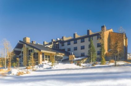 Snow-covered luxury mountain hotel with clear blue sky and surrounding pine trees in winter scenery