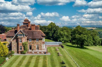 Stunning countryside manor surrounded by lush gardens and rolling hills under a sunny, cloudy sky