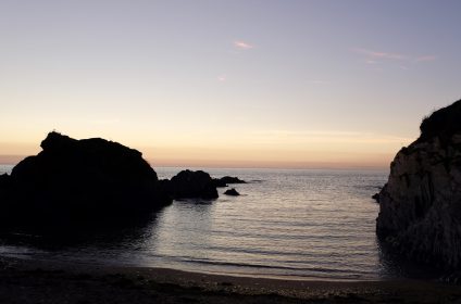 Tranquil seaside at dusk with silhouetted rocks and a soft gradient sky over calm waters