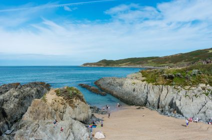 Scenic view of Woolacombe rocky beach cove with people enjoying the sea and coastline under a bright blue sky