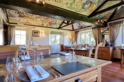 Elegant restaurant interior with rustic wooden tables and chairs, featuring artistic ceiling and large windows with curtains
