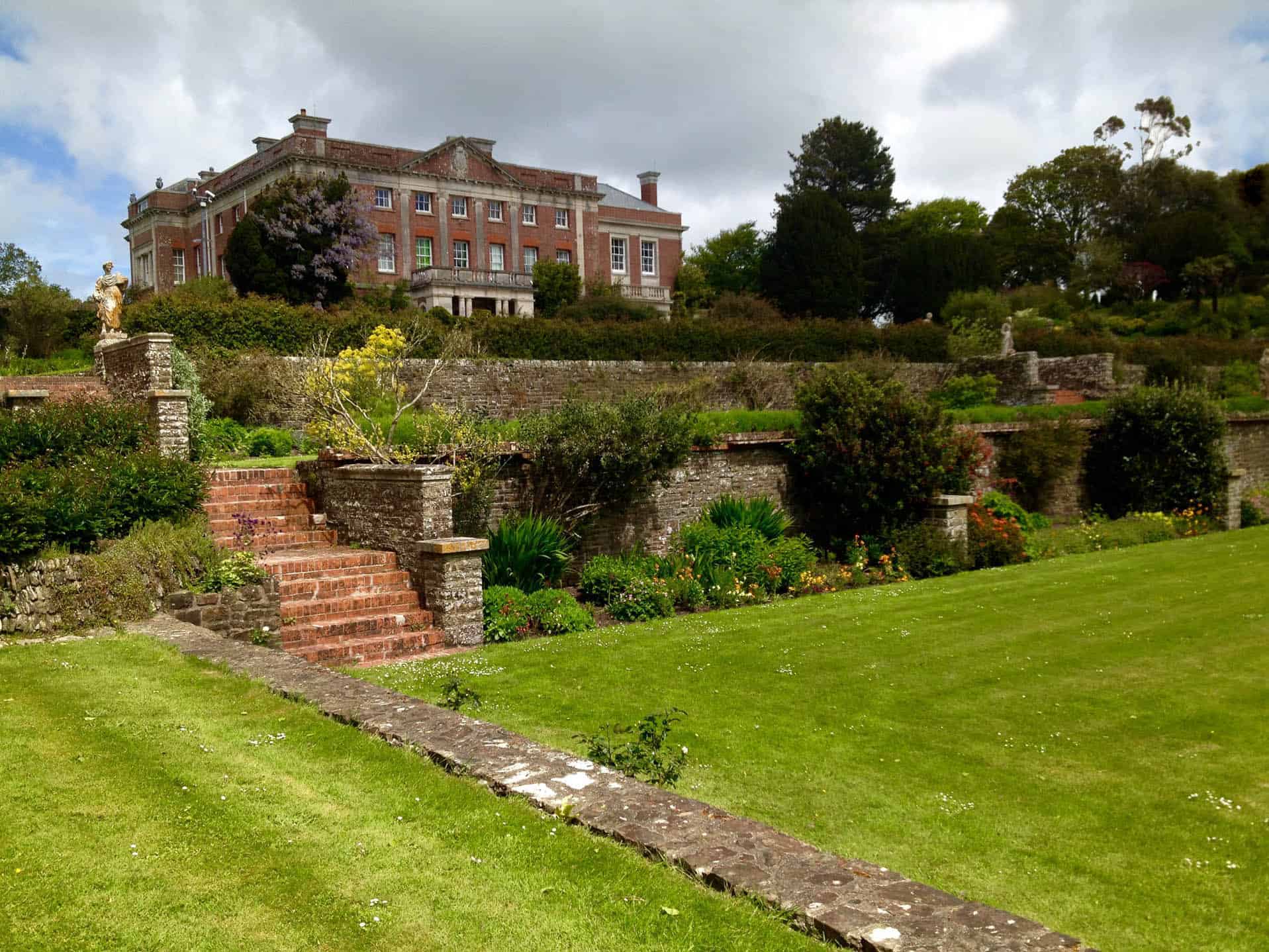 Historic English mansion with stunning landscaped gardens and stone pathways under a cloudy sky