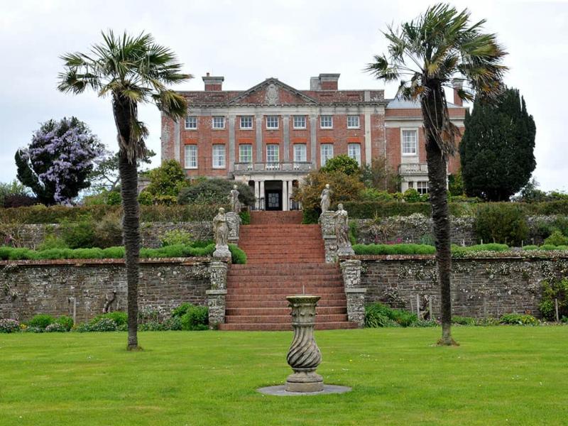 Historic mansion with elegant gardens, palm trees, and stone steps in lush green setting, perfect for heritage tours