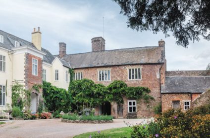 Historic English manor with ivy-clad brick facade, surrounded by lush gardens and expansive landscape