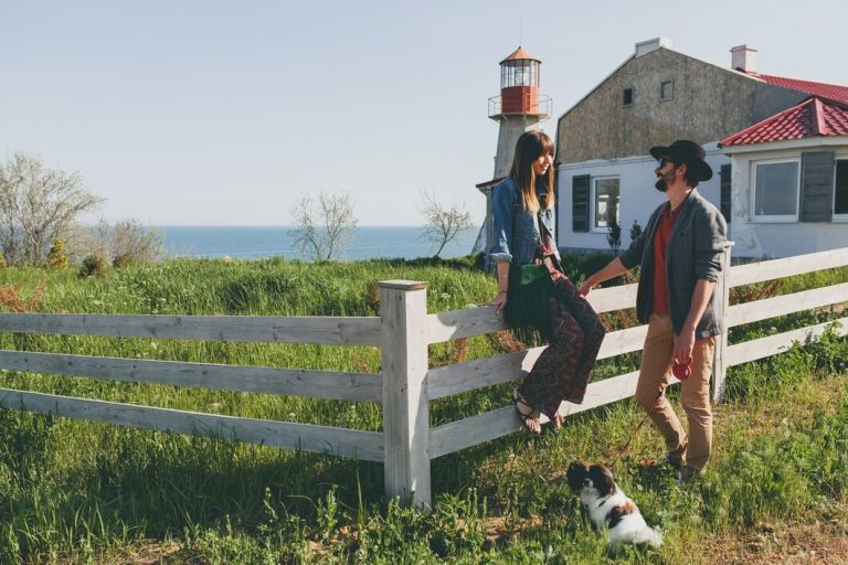Couple standing on a fence near a lighthouse, accompanied by their dog, enjoying a scenic coastal view