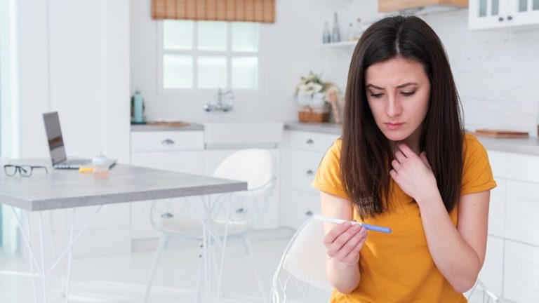 A woman sitting in a kitchen, holding a thermometer and checking the temperature of a dish